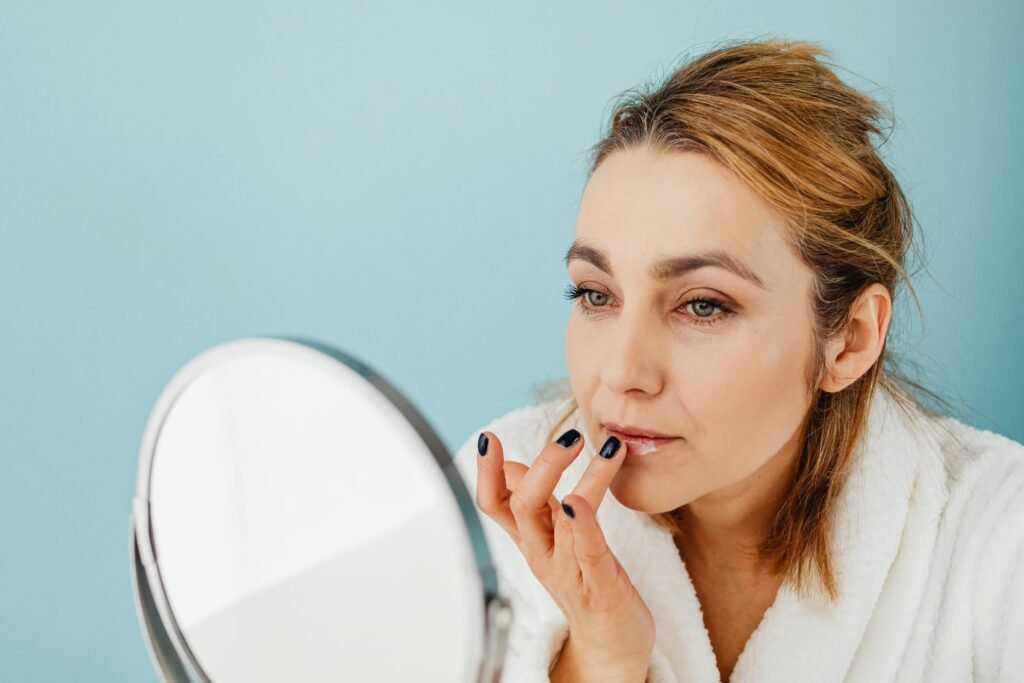 A woman in a bathrobe applies lip balm while looking in a mirror, highlighting skincare and self-care.