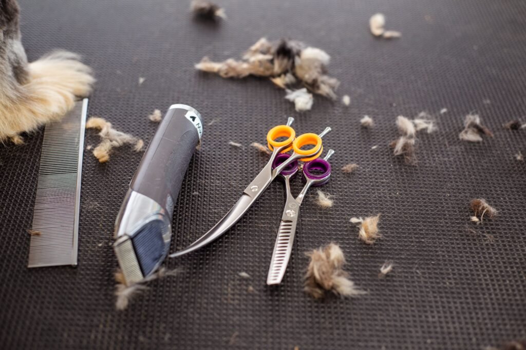 Close-up of grooming tools including scissors, trimmer, and pet fur on a black mat.