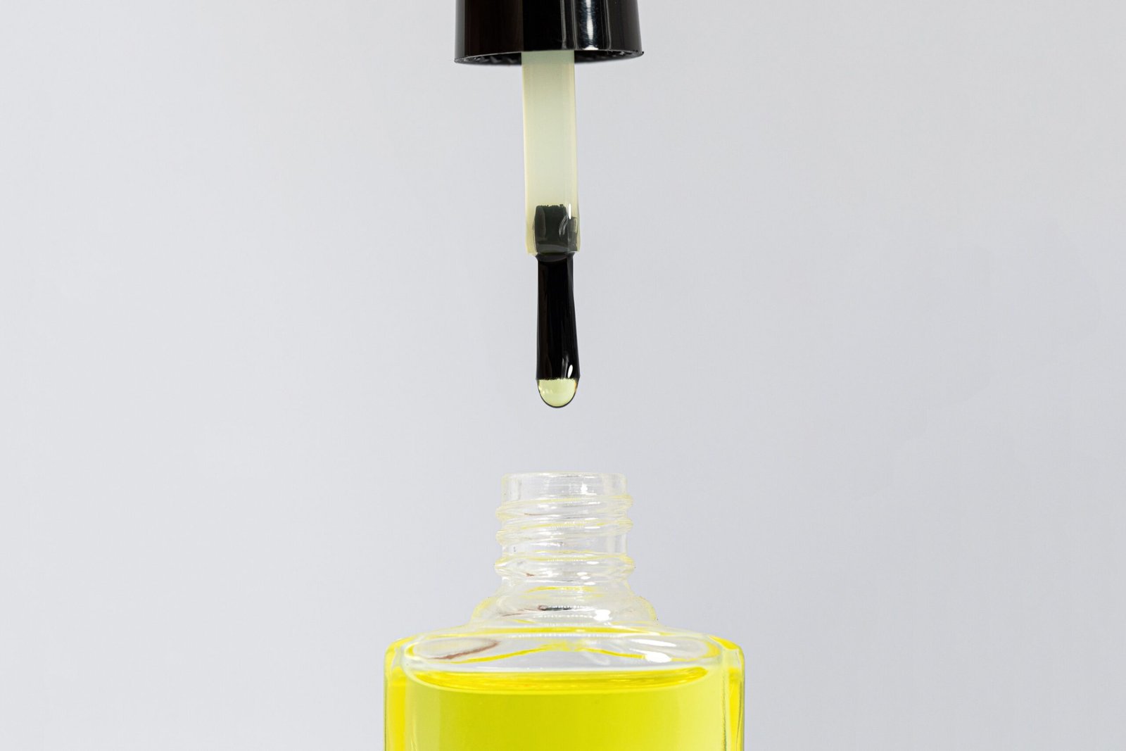 Focused shot of a nail care dropper dripping oil into a bottle against a neutral background.