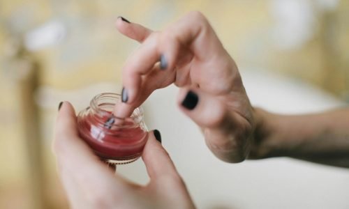 Close-up of a woman applying balm from a glass jar, focusing on skincare aesthetics.